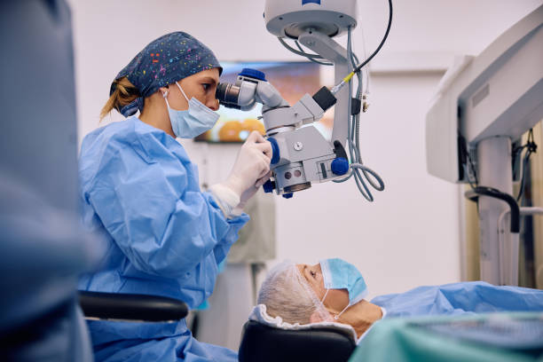 Ophthalmologist looking through microscope during eye surgery of mature patient at the clinic.